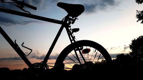 Low angle view of silhouette bicycle on field against sky at sunset