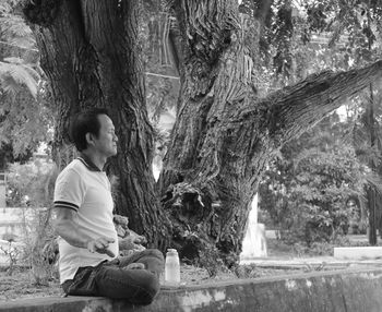 Side view of mature man meditating on retaining wall by tree