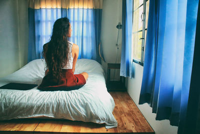 Rear view of woman sitting on bed