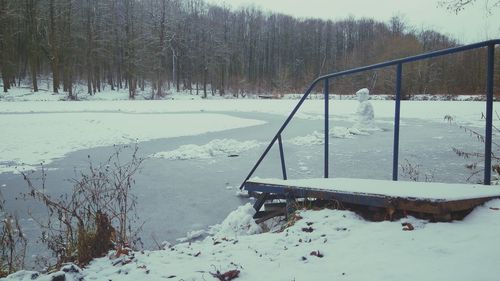 Snow covered field by lake against sky