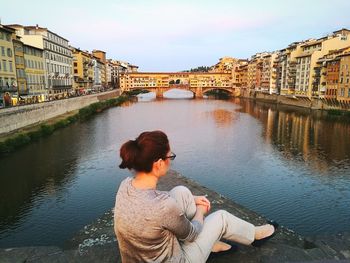 Woman sitting on bridge over river in city