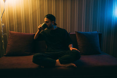 A young man drinks tea sitting on a sofa