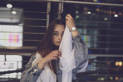 Portrait of young woman holding fabric against metal fence