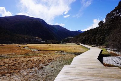 Empty footpath leading towards mountains against sky