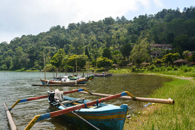 Boats moored on river amidst trees against sky