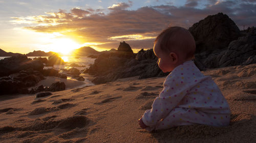 Baby boy on beach against sky during sunset