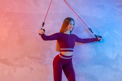 Woman pulling straps against wall in health club