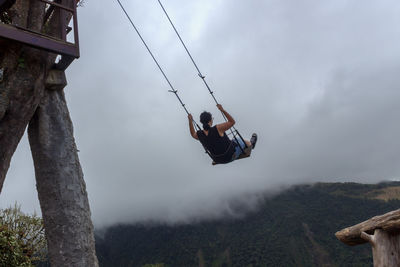 Rear view of woman playing on swing against sky