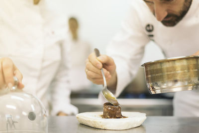 Midsection of chef garnishing food on table in kitchen