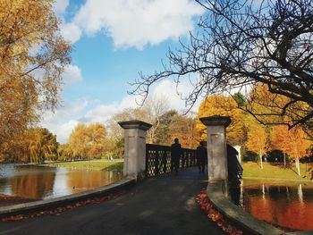 Walkway by lake against sky during autumn