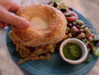 Close-up of hand holding bagel on a plate