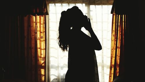 Rear view of silhouette woman standing against window