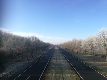 Road amidst bare trees against clear sky