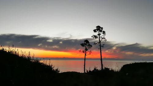 Silhouette trees by lake against romantic sky at sunset