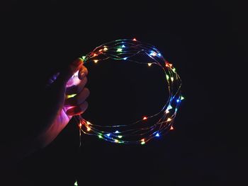 Close-up of hand holding colorful illuminated lighting equipment against black background