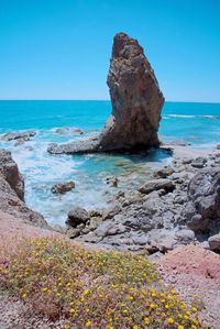 Scenic view of rocks in sea against clear blue sky