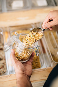 Back view of anonymous female pouring dry pasta inside glass jar in local store