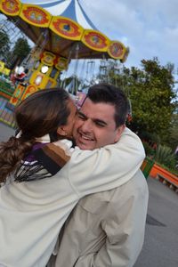 Smiling young man embraced by girlfriend in near amusement park