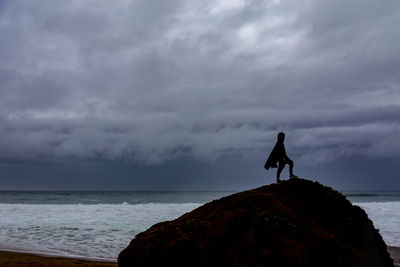 Man standing on rock by sea against sky