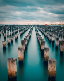High angle view of wooden posts in sea against cloudy sky during sunset