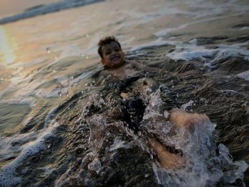 Shirtless boy swimming in sea during sunset