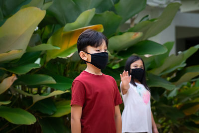 Two asian children wearing mask standing in distance of 1 meter from others keeping distancing. 