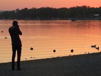 Full length of silhouette boy on lake against sky during sunset
