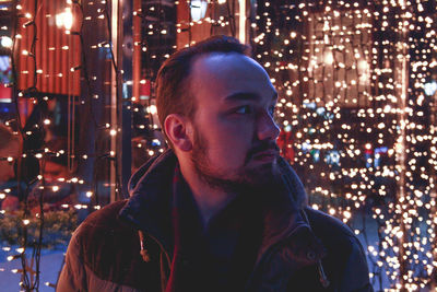 Young man looking away against illuminated lighting equipment at night