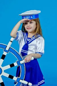 Cute girl wearing sailor uniform saluting against blue background