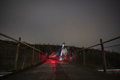 Illuminated chainlink fence against sky at night