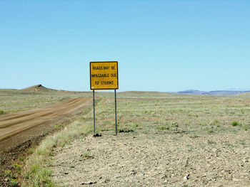Road sign on field against clear sky