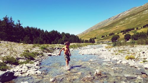 Boy wading in stream against clear sky