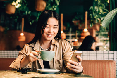 Young woman drinking coffee while sitting on table at cafe