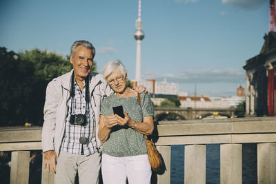 Senior man arm around standing with woman on bridge in city