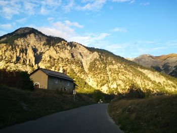 Road amidst houses and mountains against sky