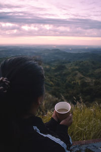 Rear view of woman looking at mountains against sky during sunrise