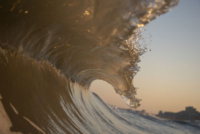 Sea waves splashing against clear sky during sunset