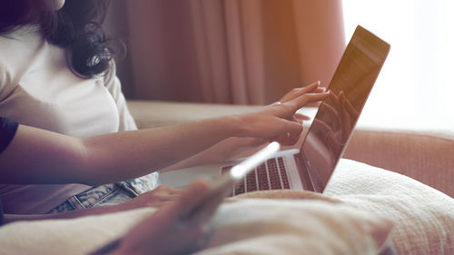 Midsection of women using laptop on bed at home