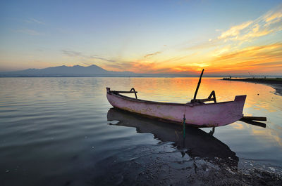 Boat moored in sea against sky during sunset