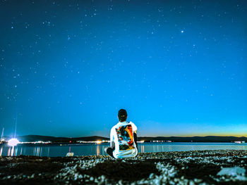 View of a young man sitting on a rocky beach, observing the scene and thinking how small we are.