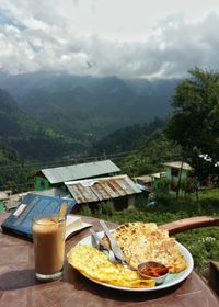 Close-up of fresh breakfast with chai by novel on table at sidewalk cafe against mountains