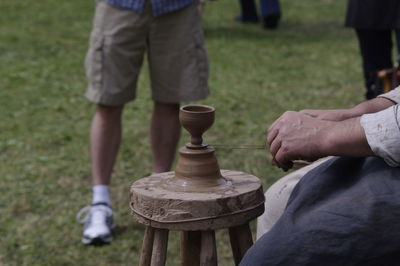 Midsection of man molding clay on stool at field