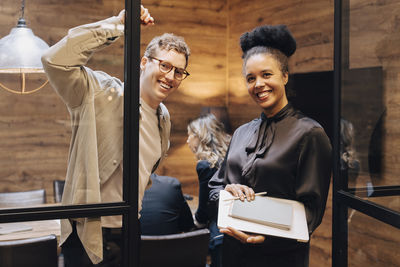 Portrait of smiling businessman and businesswoman standing at board room doorway in office