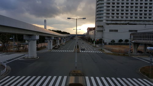 Road amidst buildings in city against sky during sunset