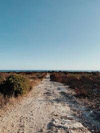 Dirt road amidst land against clear sky
