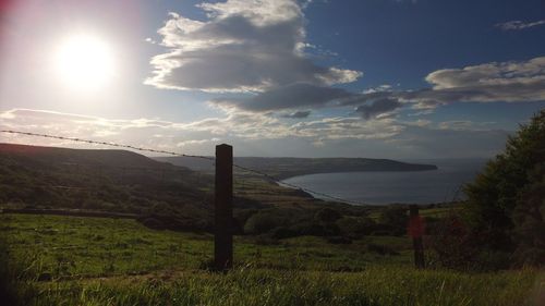 Scenic view of field by sea against sky