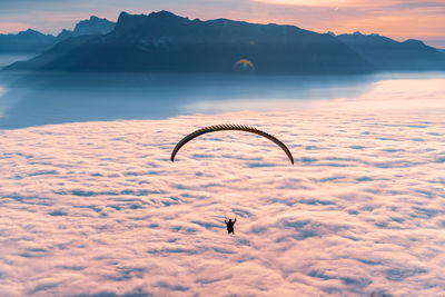 Silhouette of person paragliding over cloudscape