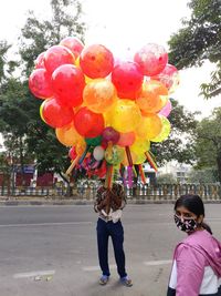 People with multi colored balloons against trees