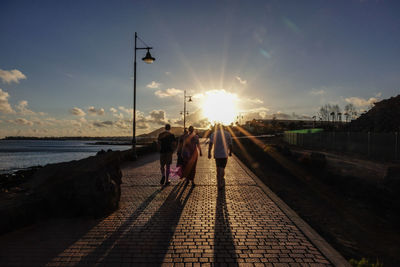 Rear view of people walking on street against sky during sunset