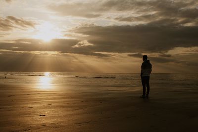Silhouette woman standing at beach against sky during sunset